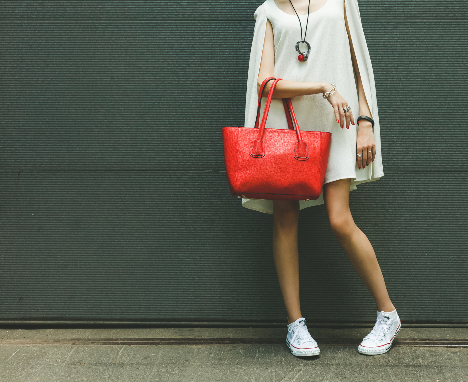 Fashionable beautiful big red handbag on the arm of the girl in a fashionable white dress, posing near the wall on a warm summer night. Warm color.